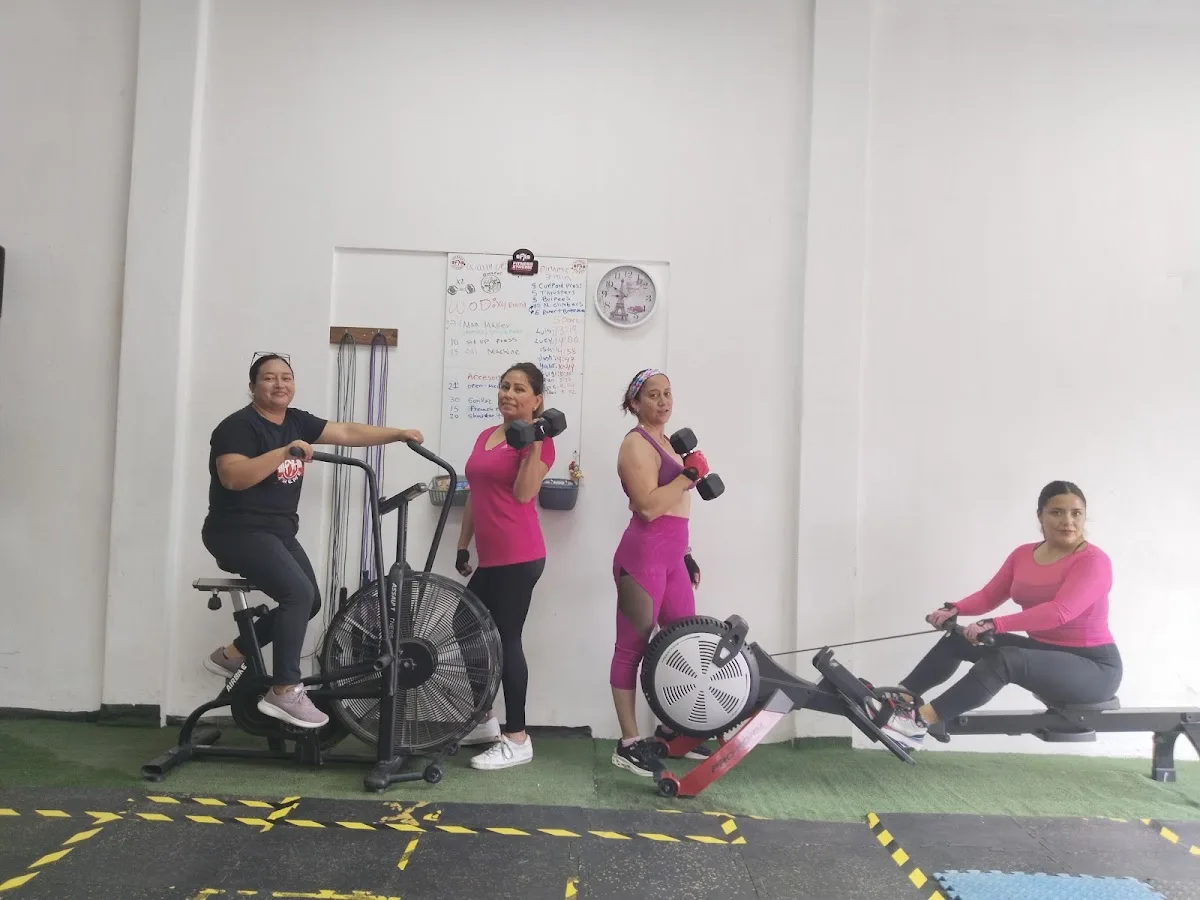 Alumnas en la bici de aire y la remadora, con el WOD en el pizarrón